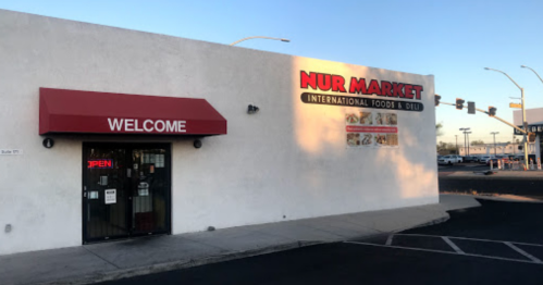 Exterior of Nur Market, an international foods and deli store, featuring a red awning and an "OPEN" sign.