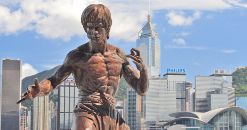 A bronze statue of a martial artist against a city skyline, showcasing strength and dynamic movement.