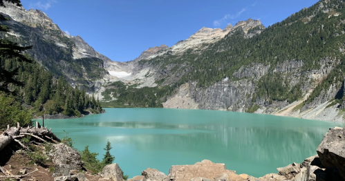 A serene turquoise lake surrounded by mountains and lush greenery under a clear blue sky.