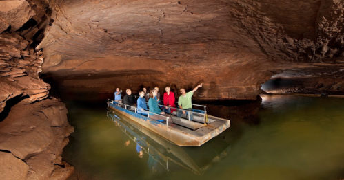 A group of people on a boat exploring a cave with rock formations and water reflections.