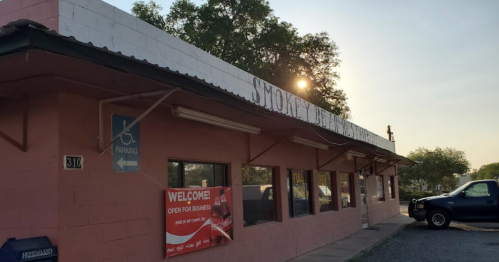 Exterior of a pink building with a sign reading "Smokey's" and a parked blue truck, under a sunset.