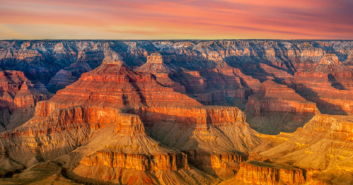 Vibrant sunset over the Grand Canyon, highlighting its layered rock formations and dramatic cliffs.