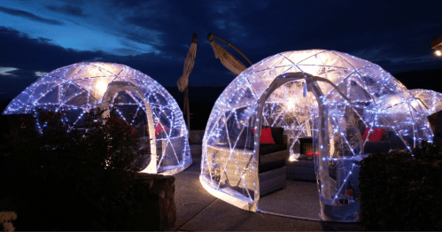 Two illuminated igloo-shaped structures with fairy lights, set against a twilight sky, creating a cozy outdoor atmosphere.