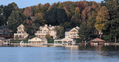 A serene lakeside view featuring charming homes and colorful autumn trees reflecting on the water.