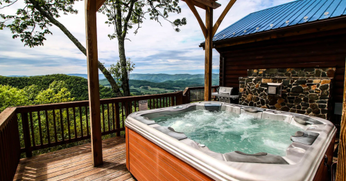 A hot tub on a wooden deck with a scenic view of mountains and trees under a blue sky.