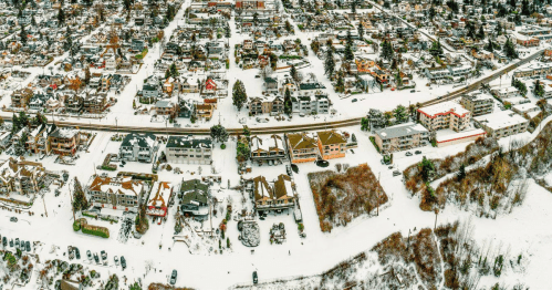 Aerial view of a snow-covered town with residential buildings, roads, and trees blanketed in white.