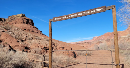 Sign for "Lonely Dell Ranch Historic District" at a desert landscape with rocky hills and clear blue sky.