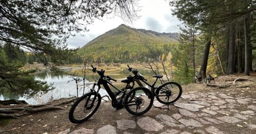 Two mountain bikes parked on a stone path, with a scenic view of a lake and forested hills in the background.