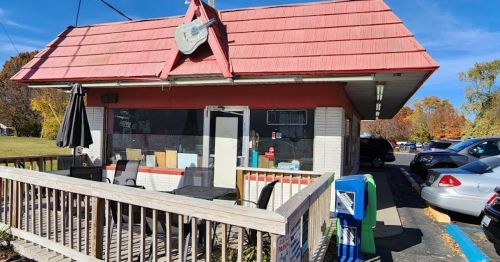 A small, red-roofed building with a guitar sign, featuring outdoor seating and an "Open" sign.