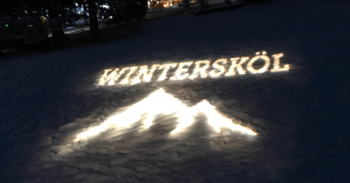 Illuminated text "WINTERSKÖL" and mountain silhouette on a snowy ground at night.