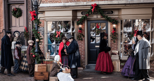 A festive street scene with people in Victorian attire, holiday decorations, and a shop called "Cobblestone Gifts."