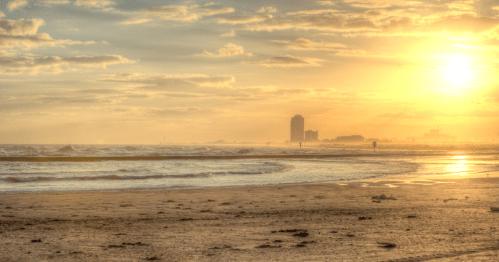 A serene beach at sunset, with gentle waves and a distant skyline under a golden sky.