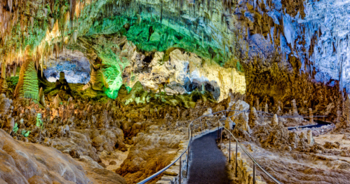 A colorful cave interior with stalactites and stalagmites, featuring a winding pathway for visitors.