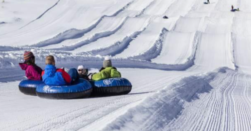 A group of people in colorful winter jackets tubing down a snowy slope on inflatable tubes.