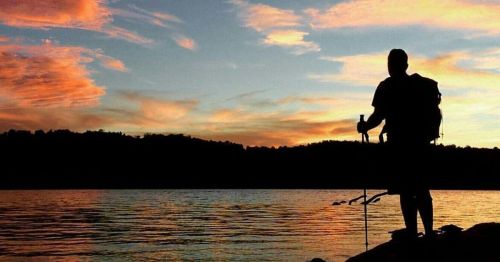 Silhouette of a hiker by a lake at sunset, with vibrant clouds reflecting on the water.