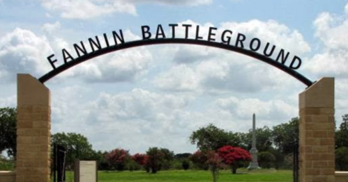 Archway sign reading "Fannin Battleground" with trees and a monument in the background under a cloudy sky.