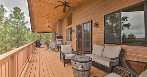 A wooden deck with seating, a table, and a grill, surrounded by trees under a cloudy sky.