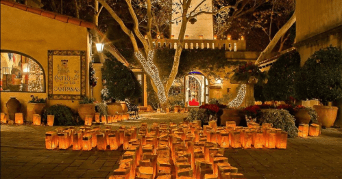 A beautifully lit courtyard with glowing lanterns, festive decorations, and trees adorned with lights at night.