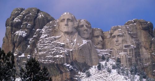 Mount Rushmore featuring the carved faces of four U.S. presidents on a rocky mountain, surrounded by trees and snow.