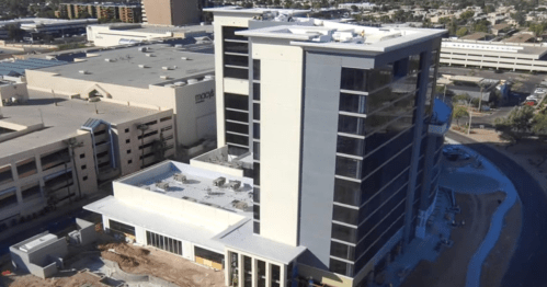 Aerial view of a modern multi-story building under construction, surrounded by other structures and a clear sky.