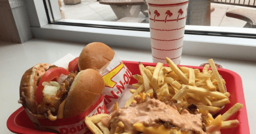 A red tray with two burgers, a serving of fries, and a drink, all set against a window view.