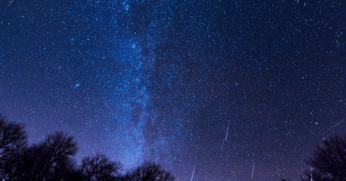 A starry night sky filled with stars and a visible Milky Way, with shooting stars streaking across the scene.