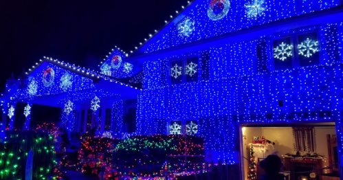 A house decorated with vibrant blue and multicolored Christmas lights, featuring snowflake designs and festive displays.