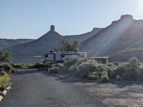 A camper parked near a serene landscape with mountains and greenery under a clear sky.