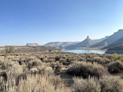 A serene landscape featuring a lake surrounded by mountains and dry shrubs under a clear blue sky.