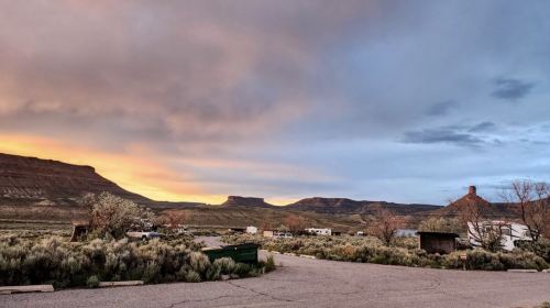 Sunset over a desert landscape with mountains, shrubs, and a few parked RVs in the foreground.