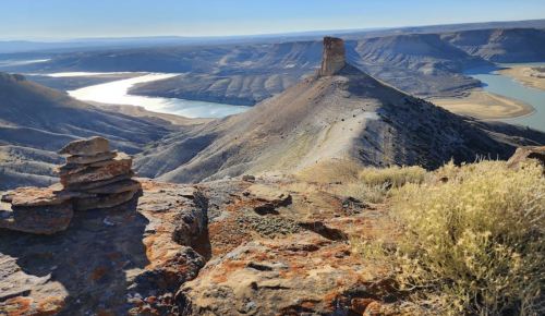 A scenic view of a river winding through rugged mountains, with a rock formation in the foreground and clear blue skies.