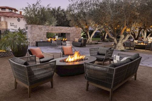 Cozy outdoor seating area with a fire pit, surrounded by olive trees and soft lighting at dusk.