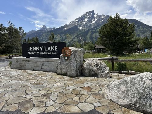 Sign for Jenny Lake in Grand Teton National Park, with mountains and trees in the background on a sunny day.