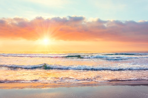 A serene beach scene at sunset, with gentle waves and a vibrant sky filled with orange and pink hues.