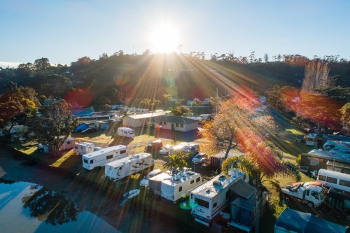 Aerial view of a campsite with RVs and trees, illuminated by sunlight streaming through the morning sky.