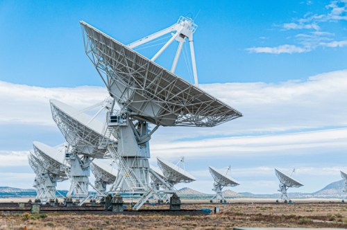 A row of large satellite dishes facing the sky against a blue sky and distant mountains.