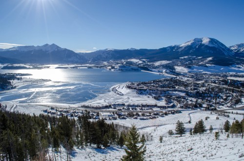 A scenic winter landscape featuring a frozen lake, snow-covered mountains, and a small town nestled in the valley.