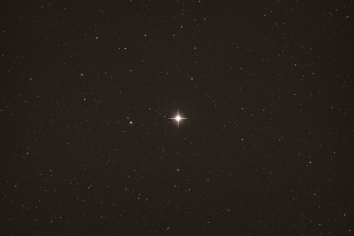 A bright star surrounded by a field of distant stars against a dark night sky.