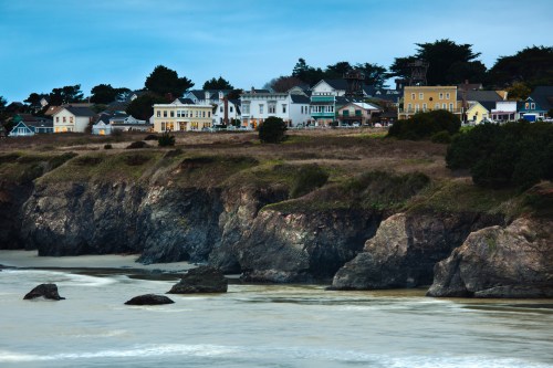 Coastal view of a rocky shoreline with colorful houses perched on a cliff under a cloudy sky.