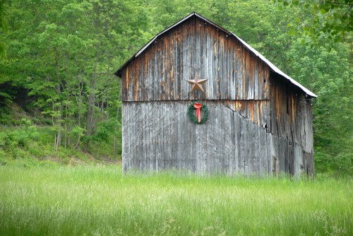 A rustic wooden barn with a star and a wreath, surrounded by lush green grass and trees.