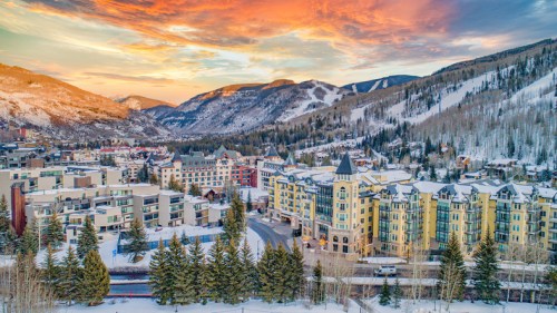 A scenic winter landscape featuring snow-covered mountains and a colorful sunset over a charming village.