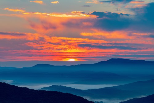 A vibrant sunset over rolling mountains, with colorful clouds and a misty valley below.