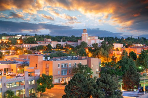 A scenic view of a city at dusk, featuring buildings, trees, and a colorful sky with clouds.