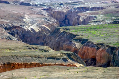 A vast, rugged landscape featuring deep canyons and rocky terrain, with patches of green vegetation.