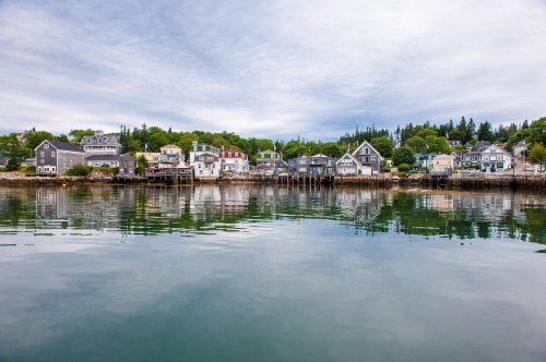 A serene waterfront view of colorful houses reflecting in calm water under a cloudy sky.