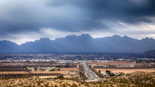 A panoramic view of a valley with a highway, surrounded by mountains under a cloudy sky.