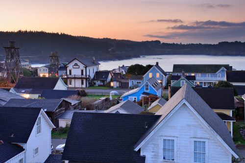 A coastal town at sunset, featuring colorful houses and a serene bay with distant hills.