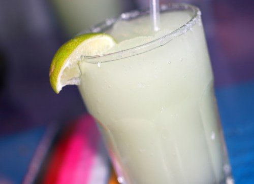 A refreshing cocktail in a glass with a salted rim and a lime wedge, set against a colorful background.