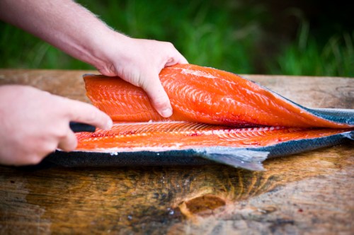 A person filleting a fresh salmon on a wooden surface, showcasing the bright orange flesh.