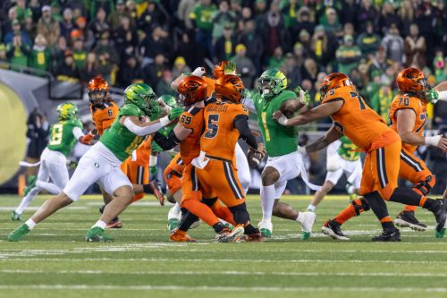 A football game scene with players in green and orange uniforms engaged in a play on the field.